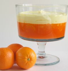 two oranges sitting next to an orange dessert in a glass dish on a table