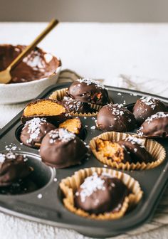 there are chocolates in the muffin tin and one is being dipped with powdered sugar