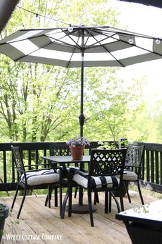 an outdoor table and chairs on a deck with an umbrella over the dining room table