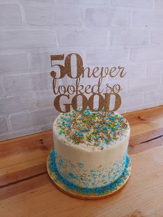 a white cake with blue and gold sprinkles sitting on top of a wooden table