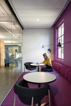 a man is sitting at a table in an office setting with purple walls and black chairs