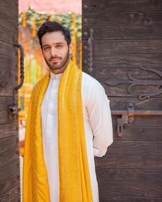 a man standing in front of a wooden door wearing a white shirt and yellow scarf