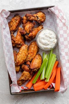 chicken wings, celery and carrots with ranch dressing in a tray on a table