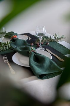 a place setting with green napkins, silverware and greenery on the table