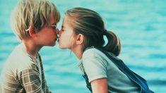 two little kids kissing each other on the beach with water in the backgroud