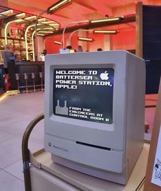 an apple computer sitting on top of a counter in a building with people standing around