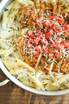 pasta with chicken, tomatoes and parmesan cheese in a white bowl on a wooden table