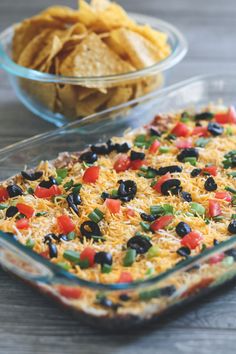 a casserole dish filled with black olives, peppers and cheese next to a bowl of tortilla chips