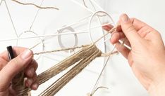 two hands are holding twine and making a piece of string art with the letter o on it