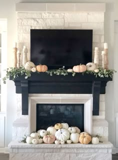 a fireplace mantel with white pumpkins and greenery on it, next to a flat screen tv