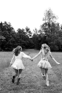 two girls are running in the grass holding hands