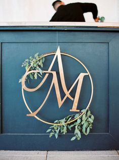 a man standing behind a blue counter with a gold monogrammed sign on it