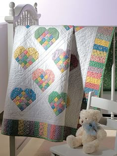 a teddy bear sitting on a chair next to a quilted heart - shaped blanket