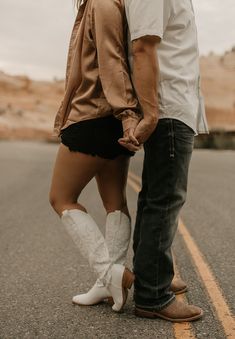 a man and woman holding hands while standing on the side of an empty road together