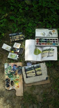 an open book sitting on top of a wooden table next to paint and watercolors