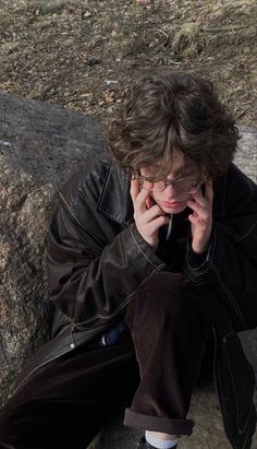 a young man sitting on the ground talking on his cell phone while holding his hand to his face