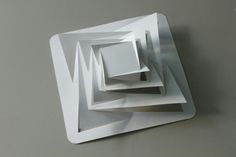 a white square shaped object hanging on the wall next to a gray wall with an abstract design