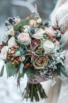 a bride holding a bouquet of flowers and greenery on her wedding day in the snow