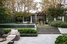 an outdoor living area with seating and trees in the back yard, surrounded by shrubbery