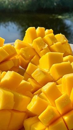 sliced mangoes are sitting on a white plate near the water and trees in the background