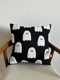 a black pillow with white ghost faces on it, sitting on a chair in front of a wall