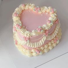 a heart shaped cake with pink frosting and flowers on it's sides, sitting on a white surface