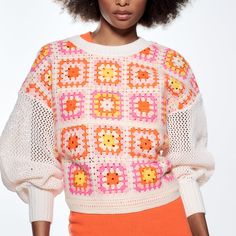 a woman with an afro standing in front of a white background wearing a colorful sweater