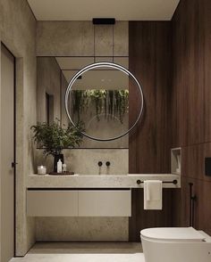 a white toilet sitting next to a bathroom sink under a round mirror in a bathroom