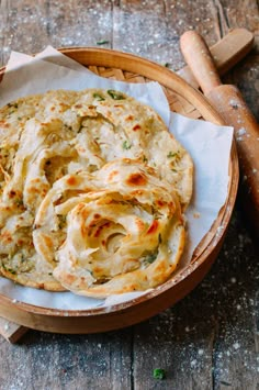 two flat breads in a wooden bowl on a table next to a rolling pin