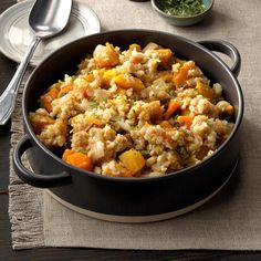 a pan filled with rice and vegetables on top of a table next to silverware