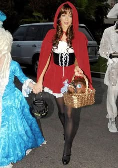 three people in costumes are walking down the street with one holding a basket and another carrying a purse