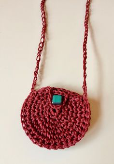 a crocheted red purse hanging from a chain on a white surface with a turquoise stone in the center