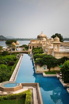 an outdoor swimming pool surrounded by greenery and water features in front of a palace like building