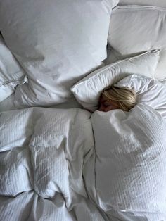 a woman laying in bed with white sheets and pillows on top of her head as she sleeps