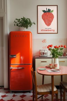 an orange refrigerator sitting next to a table with flowers on it and a potted plant