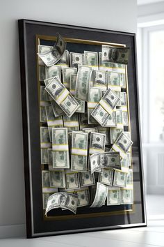 a black frame filled with money sitting on top of a white floor next to a window