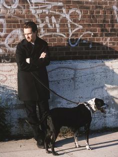 a man standing next to a dog on a leash near a brick wall with graffiti