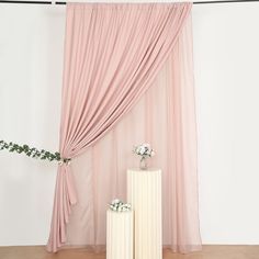 two white vases with flowers on them in front of a pink drapeed curtain