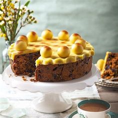 a cake sitting on top of a white cake plate next to a cup of coffee