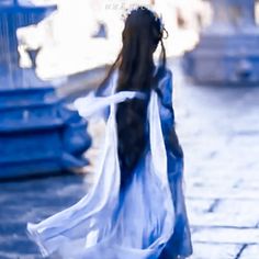 a woman with long hair wearing a white dress walking down a street in the rain