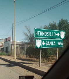 two green street signs sitting on the side of a road next to a dirt road