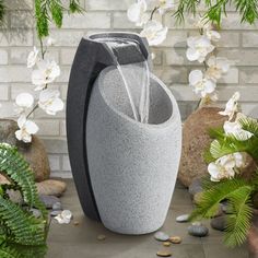 an outdoor fountain is shown in front of some plants and rocks with white flowers around it