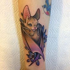 a cat is sitting in a bat tattoo on the leg