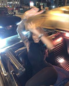 a woman sitting in the drivers seat of a car with her hands up and smiling