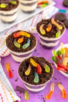 three dessert cups with gummy bears in them on a purple tablecloth next to other cupcakes