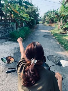 a woman riding on the back of a motorcycle down a dirt road