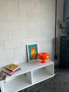 an orange vase sitting on top of a white shelf next to a book case and speakers