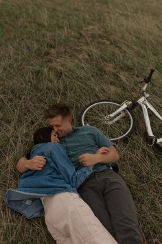 a man laying on the ground next to a bike and kissing his girlfriend's forehead