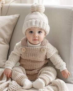 a baby is sitting on a couch wearing a knitted outfit and hat with buttons