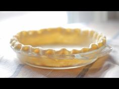 a pie crust sitting in a glass dish on a tablecloth with a window behind it